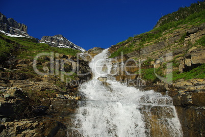 Waterfall, snow mountains and intense blue sky near Logan Pass,Glacier National Park,Montana