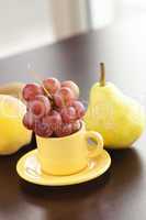 peach, pear, grapes in a cup and saucer on a wooden table