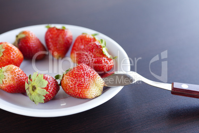 strawberries on a plate and spoon on a wooden table