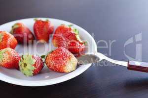 strawberries on a plate and spoon on a wooden table