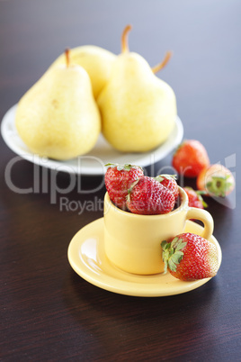 strawberries, pears on a plate and cup with saucer on a wooden t