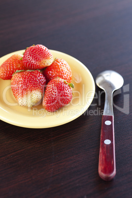 strawberries on a plate and spoon on a wooden table