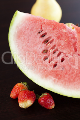 Watermelon, strawberry and pear lying on a wooden table