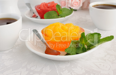 A cup of coffee and orange jelly with slices of fresh orange