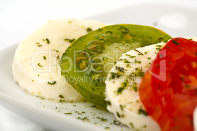 Tomatenscheiben und Mozzarella mit Kräutern und Olivenöl auf einem Teller vor weißem Hintergrund