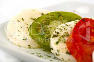 Tomatenscheiben und Mozzarella mit Kräutern und Olivenöl auf einem Teller vor weißem Hintergrund