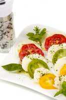Tomatenscheiben und Mozzarella mit Basilikum auf Teller vor weißem Hintergrund