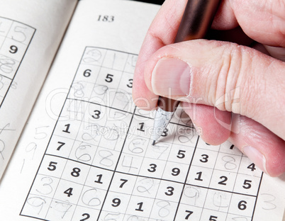 Man hand holding pencil on sudoku puzzle