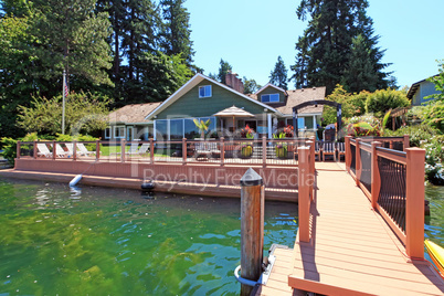 Lakefront green one story house with dock and large deck.