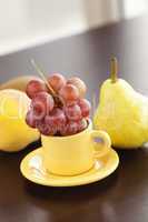 peach, pear, grapes in a cup and saucer on a wooden table