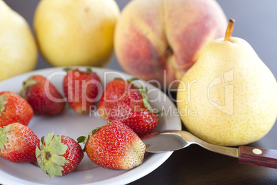 strawberry  in plate,spoon, pear and peach on a wooden table