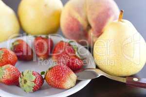 strawberry  in plate,spoon, pear and peach on a wooden table