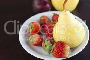 strawberry  in plate, pear and peach on a wooden table
