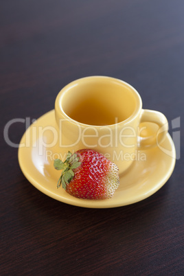 strawberries and a cup with saucer on a wooden table