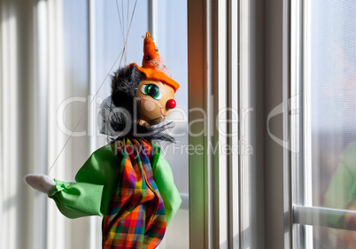 String puppet gazing outside window in sun