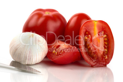 Frische Tomaten mit Messer und Knoblauchzwiebel vor weißem Hintergrund