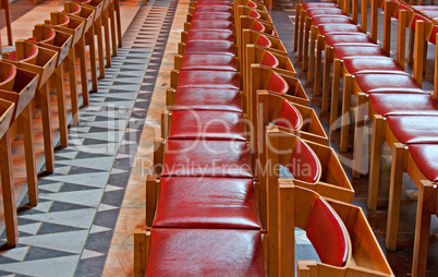 Rows of red backed wooden chairs in church