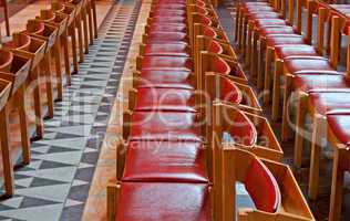 Rows of red backed wooden chairs in church