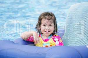 Baby girl having fun on a blue float into a tropical swimming po