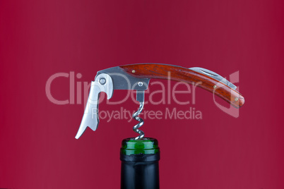 Korkenzieher in Weinflasche vor rotem Hintergrund