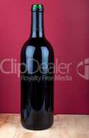 Weinflasche auf Holzplatte vor rotem Hintergrund