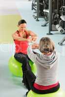 Senior woman with trainer stretching fitness ball
