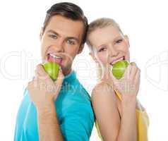 Young couple posing back to back with green apples