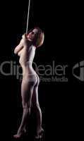 nude woman stand with rope on hands in dark