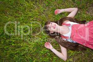Pretty girl in red sarafan lies on the green grass