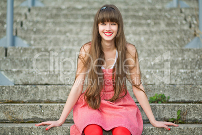 Beautiful girl in a red dress sitting on the gray concrete steps