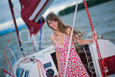 Beautiful girl in light dress standing on the deck of sailboat