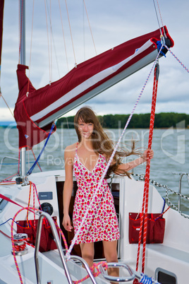 Beautiful girl in light dress standing on the deck of sailboat
