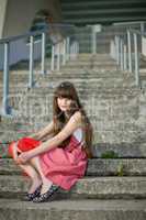 Beautiful girl in a red dress sitting on the gray concrete steps