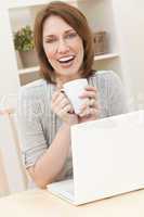 Woman Using Laptop Computer At Home Drinking Tea or Coffee