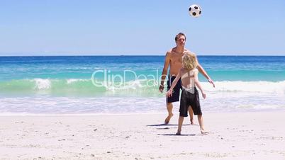 Vater und Sohn spielen Fußball am Strand