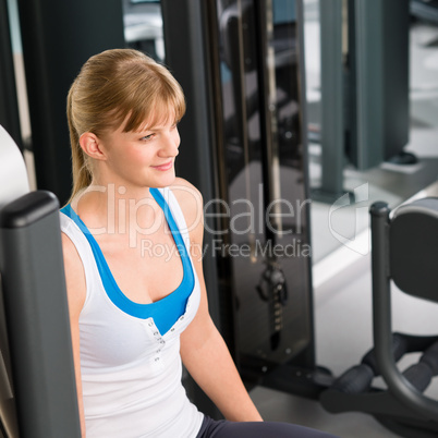 Young woman at fitness center sitting machine