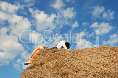 Young attractive woman on hay bale in summer field
