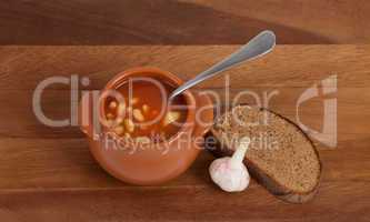Soup in clay pot with bread and garlic