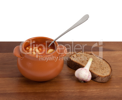 Soup in clay pot with bread and garlic on wooden table
