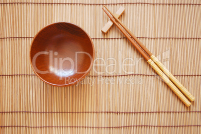 Chopsticks with wooden bowl on bamboo matting background