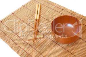 Chopsticks with wooden bowl on bamboo matting background