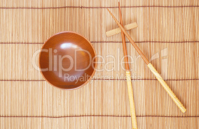 Chopsticks with wooden bowl on bamboo matting background