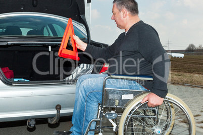 Man in a wheelchair and warning triangle next to his car