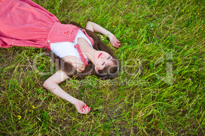 Pretty girl in red sarafan lies on the green grass