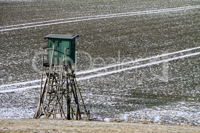 Feld mit Schneespuren und Hochsitz