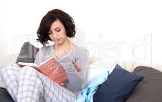 beautiful woman is sitting on the sofa an reading a book