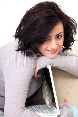 young beautiful brunette woman is sitting on a sofa with a notebook