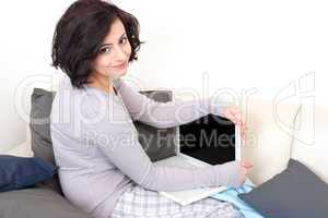young beautiful brunette woman is sitting on a sofa with a notebook