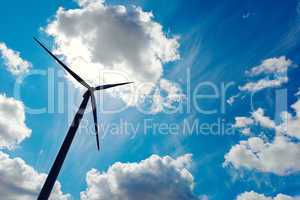 Modern wind energy turbine power station under blue sunny sky with many clouds