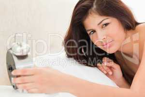 Woman is lying on a bed with a clock in her hand and is looking
